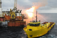 A yellow PSV putting out a fire shooting from an offshore oil rig.